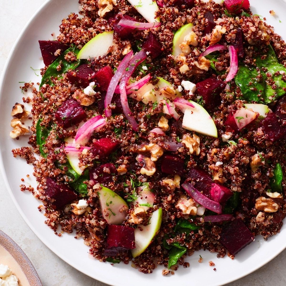 Leuchtender Quinoa-, Rote-Bete- und grüner Apfelsalat. Ein sättigendes und gesundes Mittagessen, garniert mit Nüssen und Feta.