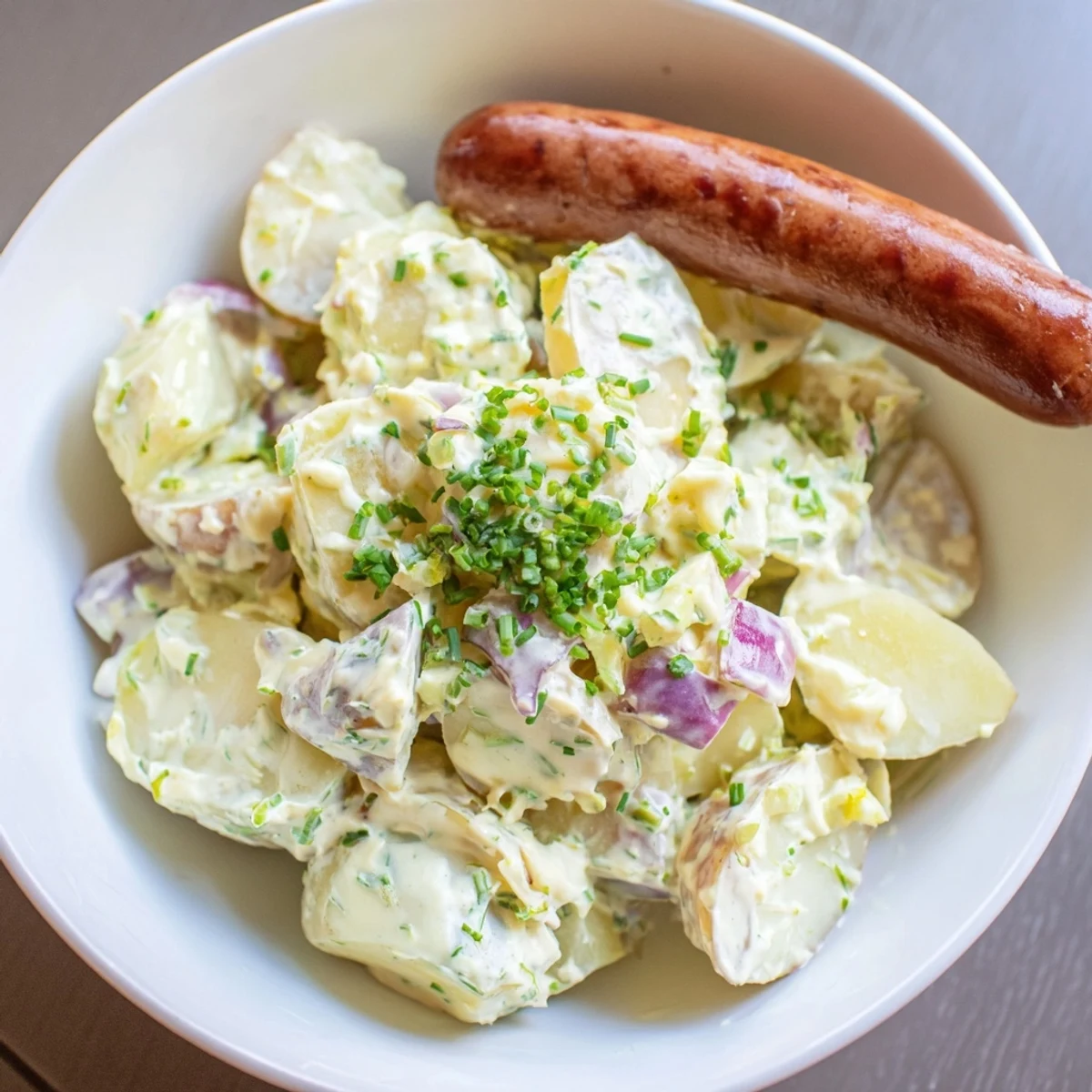 Warm potato salad with sausages, garnished with chives, ready to serve for a family meal.