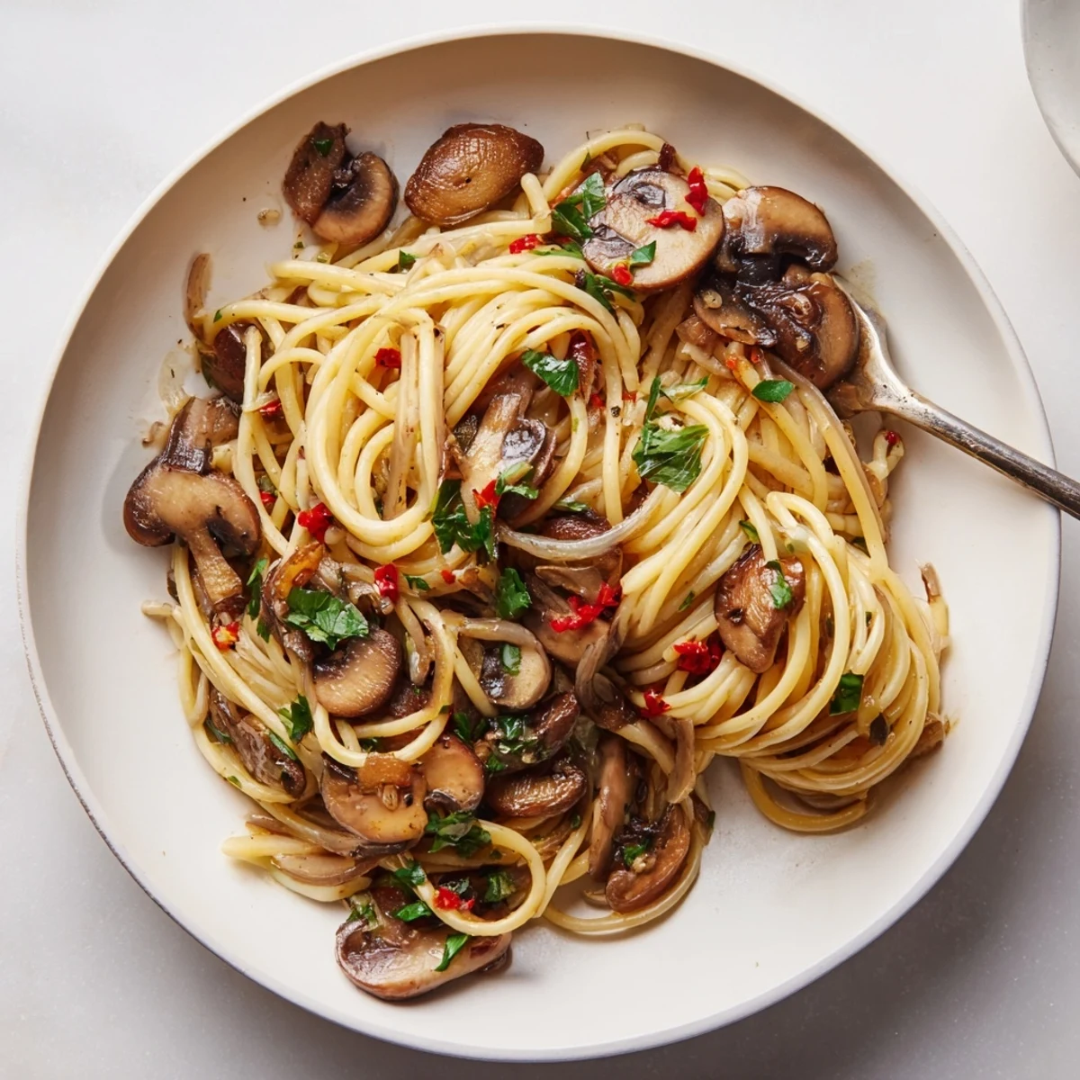 Steaming bowl of Pasta Aglio e Olio with Mushrooms, garlic, and parsley, ready to eat.