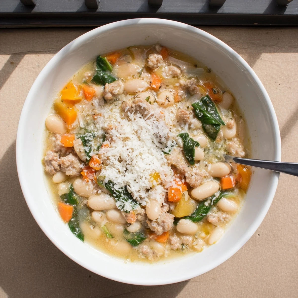 Epic Creamy Tuscan White Bean Soup With Sausage in a rustic bowl, topped with Parmesan and wilted spinach.