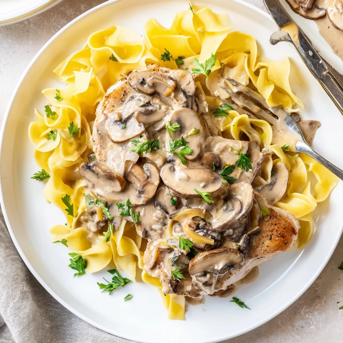 Reichhaltige Cremige Pilz-Schweinekoteletts über luftigen Eiernudeln für ein herzhaftes Abendessen.