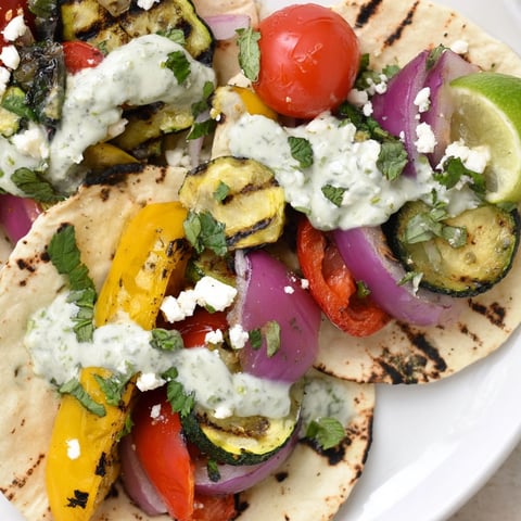 Bunte gegrillte Gemüsetacos mit Kräuter-Joghurtsauce auf warmen Maistortillas, köstliche vegetarische Mahlzeit.
