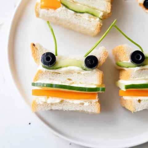 Delightful bee sandwich cutouts featuring olives, displayed with vibrant fruits and veggies at a picnic.