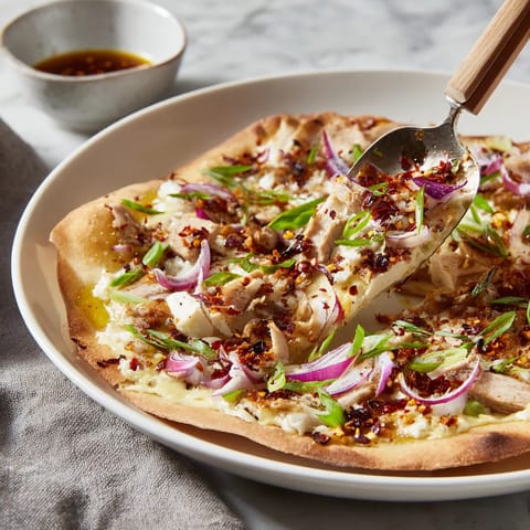 Ein Flammkuchen mit Chili-Crisp-Zutaten auf einem weißen Teller.