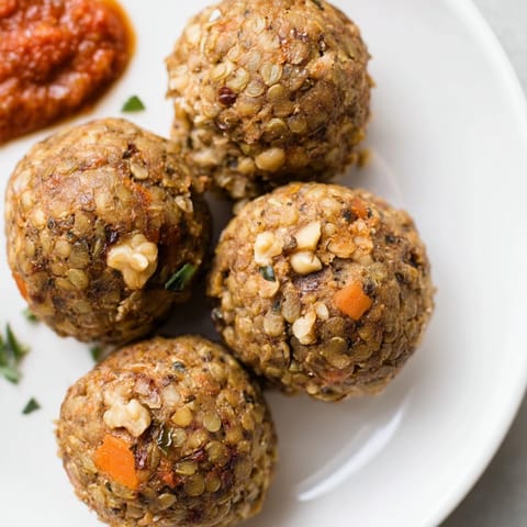 Nahaufnahme von saftigen, selbstgemachten Linsen und Walnuss-Meatballs, dampfend und bereit zum Servieren mit einer frischen Kräutersauce.