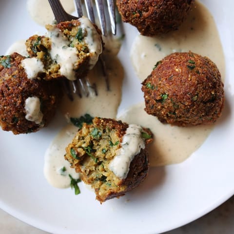 Hausgemachte Falafel mit Koriander und cremigem Tahini-Dressing, perfekt als sättigende Mahlzeit oder Vorspeise.