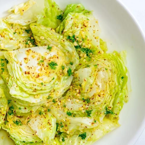 Freshly sautéed Cabbage With Garlic and Mediterranean Spices garnished with parsley and lemon wedges, served as a bright vegan side.