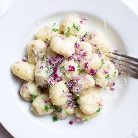 Plum Soda Gnocchi Bällchen in einer Buttersauce, garnierter mit frischen Pflaumenstücken.  