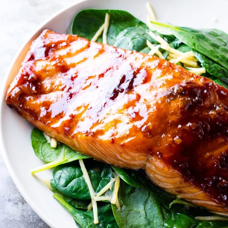 Goldbrauner Miso-Lachs liegt auf einer Schüssel sautiertem Spinat mit aromatischen Ingwerstreifen und Sojasoße.