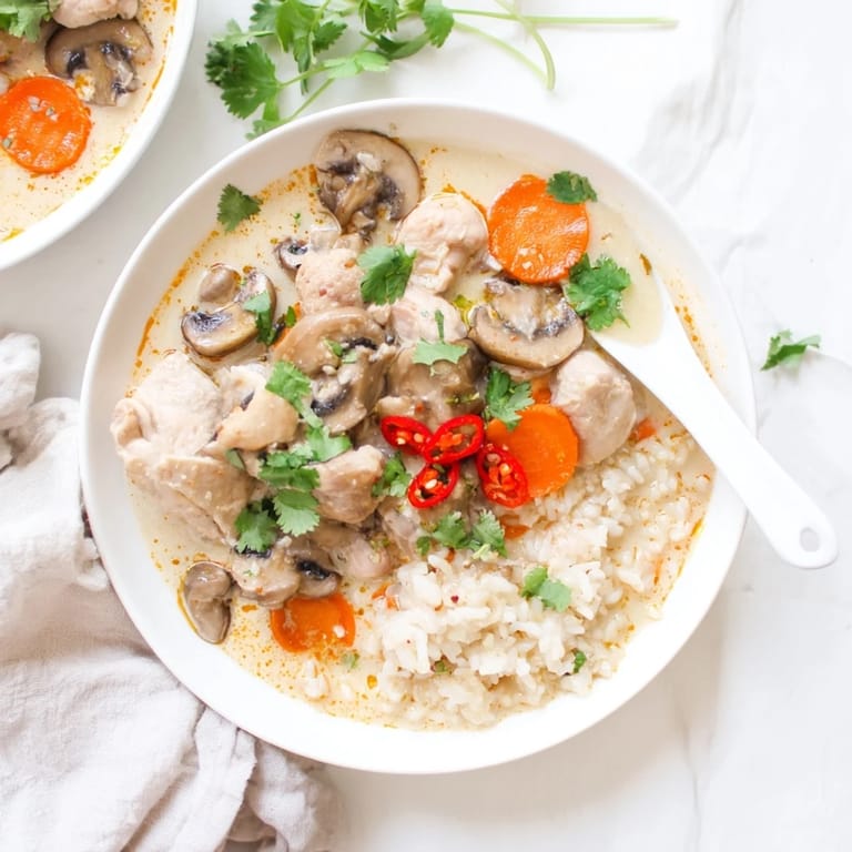 Servierbare Thai Kokos Curry Suppe, leuchtend orange, garniert mit Koriander und einer Limettenspalte.