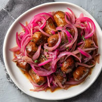 Ein weißer Teller mit sausages, die in pinken Onions eingewickelt sind, und warmem Bier.